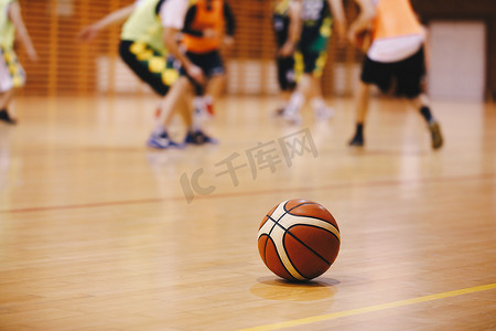 篮球训练游戏背景。篮球在木法院地板特写与模糊球员打篮球游戏在后台