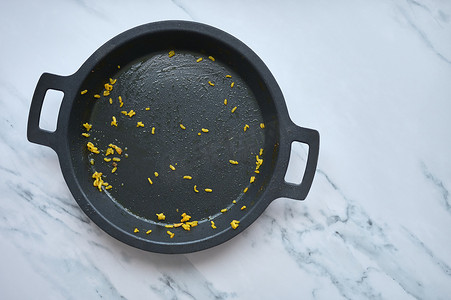 detail of an empty paella pan with leftover rice on a white marble background