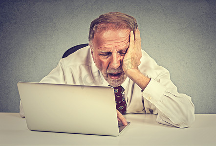 Tired sleepy senior man sitting at his desk in front of laptop computer