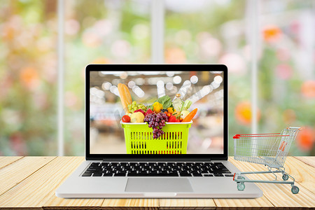 wood摄影照片_laptop computer and shopping cart on wood table with window and garden abstract blur background grocery online concept