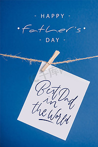 挂在绳子上摄影照片_世界上最好的爸爸的白色贺卡挂在绳子上，衣针与蓝色隔离
