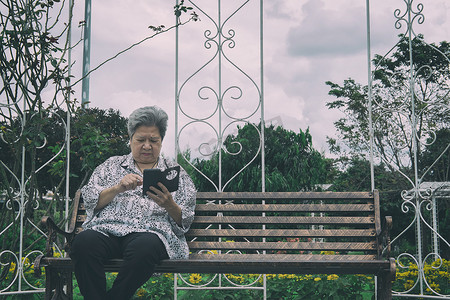 坐在长椅上的老妇人手持手机