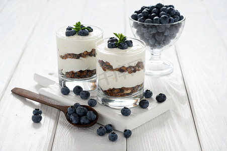 Dessert with cottage cheese, fresh blueberries and granola in a glass on a white wooden background.