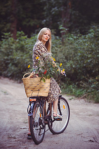漂亮的女孩穿着漂亮的连衣裙在公园里玩得很开心, 带着一辆带花的漂亮篮子。复古景观。漂亮的金发碧眼复古, 自行车和篮子花
