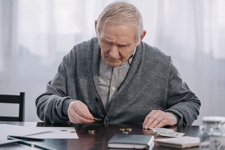 senior man sitting at table and counting money at home