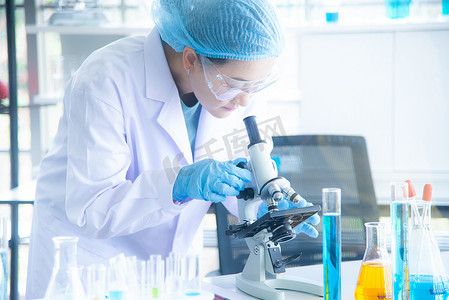 暗色显微镜摄影照片_亚洲女科学家、研究员、技术员或学生使用显微镜进行研究或实验,显微镜是医学、化学或生物实验室的科学设备