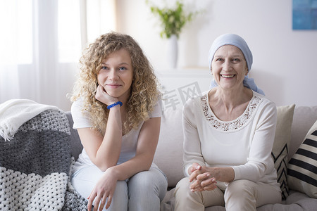 微笑的女孩和一个生病的妇女与卵巢癌坐在沙发上一起