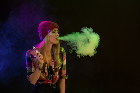 Vaping 女孩年轻的时髦女人 vape 在黑色背景上的电子香烟。嘻哈风格。工作室拍摄