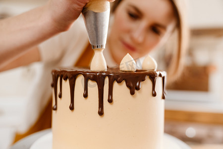 在舒适的厨房里用巧克力奶油做蛋糕的漂亮的主厨女士