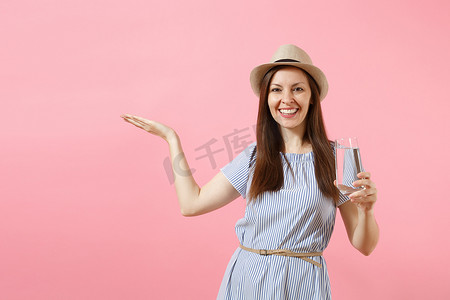 年轻美丽的女人在蓝色的礼服, 帽子持有和饮用清澈的新鲜纯净水从玻璃上的粉红色背景隔离。健康的生活方式, 人们真挚的情感观念。复制空间