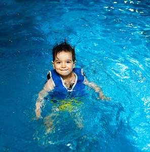 凶狠的眼神摄影照片_小男孩与充气背心在游泳池里，有一个幸福的微笑。眼神接触.