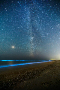 蓝色星空摄影照片_在海洋冲浪和乳白色的方式发光浮游生物的长曝光镜头。星空下水的蓝色生物发光。后部自然现象。夜空中星座中明亮的火星.