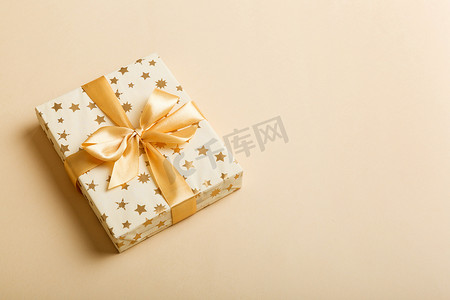 彩色圣诞节摄影照片_用白色的纸包裹着圣诞节或其他节日手工制作的礼物，背景为金色缎带。礼品盒，彩色桌上的礼品装饰，顶部有复印空间.