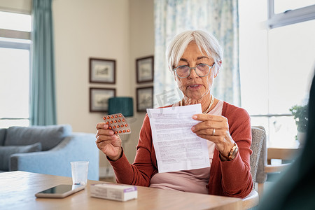 老年妇女检查处方药和药物用量。在家中吃药前，戴眼镜的老妇人先阅读医疗说明。资深女性阅读药物副作用列表及单张单张的禁忌症