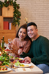 美丽的越南年轻夫妇与酒杯在新年餐桌上