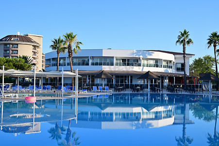 清澈蓝色水摄影照片_在土耳其的一家旅馆里，游泳池里有清澈的蓝色水。背景中的旅馆大楼反映在水中.