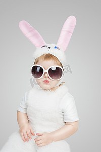 男孩穿兔子兔装和太阳镜。亲吻的嘴唇。工作室拍摄的灰色背景。2 年白色复活节兔子