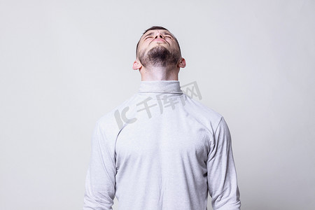 人向上看。猪鬃男装白色领毛衣衬衫抬头看着他的头上灰色背景复制空间