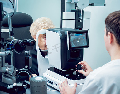 灰高级灰摄影照片_高级妇女检查她的视力与眼科医生。医疗设备。Coreometry.