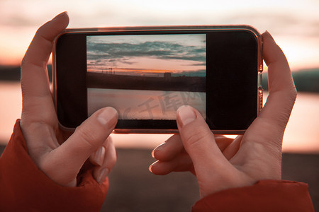 拿着照片摄影照片_妇女手拿着手机, 照片上有山湖风景.