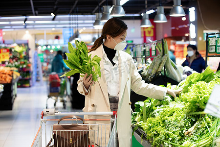 超市货架图片摄影照片_戴口罩的青年女人在超市挑选青菜