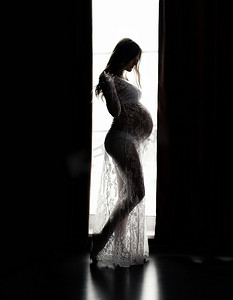 窗前一个漂亮的孕妇的侧影。美丽和柔嫩的母性