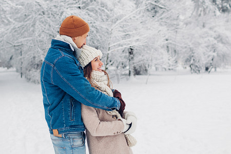 年轻貌美的恋人在冬季公园散步.在户外欣赏雪景的男女拥抱