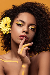 年轻感性的非洲裔美国妇女与艺术的妆, 在头发持有手指在橘色背景的嘴唇