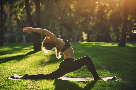 美丽的年轻女子练习瑜伽体式 Virabhadrasana 1-战士构成在公园 1 日落时分