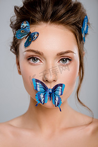 美丽的年轻女子，脸上挂着装饰蝴蝶，与灰色隔离 