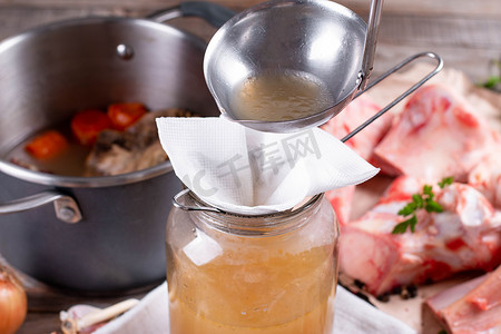 通过筛子和纸巾传递骨质肉汤.玻璃瓶中浓缩的骨肉汤