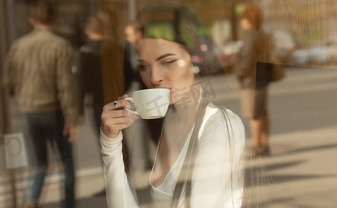 女孩拿着一个咖啡杯在当地的咖啡店, 概念照片通过窗口的城市效果与反思.