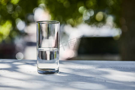 开化清水鱼摄影照片_室外的木制桌子上，阳光明媚的日子，用透明的玻璃杯盛放清水