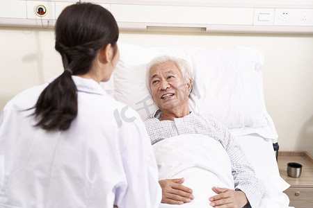 亚洲老人躺在床上与年轻的女医生交谈