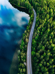 森林公路摄影照片_芬兰绿色森林与蓝色湖泊之间的公路鸟瞰图