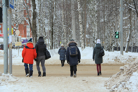在冬季城市景观的背景下，一群人穿过马路，在人行横道上看到了交通灯的绿色标志。带有空白文字和设计空间的库存照片.