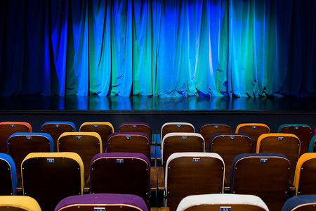 剧院观众摄影照片_剧院的礼堂舞台上的蓝绿色窗帘。多彩多姿的观众的椅子。照明设备.