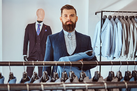 优雅的穿着胡子的男性与纹身在手和颈部选择在男装店的新服装.
