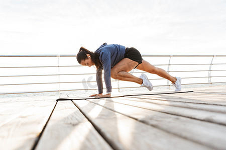 在海滩上的健身垫上做木板练习的集中运动的女运动员的侧视图