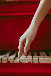 一个与女性的手与粉红的指甲弹钢琴的侧视特写。一架红色的旧钢琴，钥匙是黑白的。键盘上方的手掌。作曲家或音乐家优雅的手指