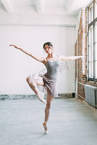 板凳摄影照片_一个年轻的芭蕾舞演员正在准备, 伸展和跳舞。在芭蕾中摆姿势。在阁楼工作室拍照片。在板凳上的俄罗斯芭蕾舞演员。芭蕾公寓和舞蹈礼服
