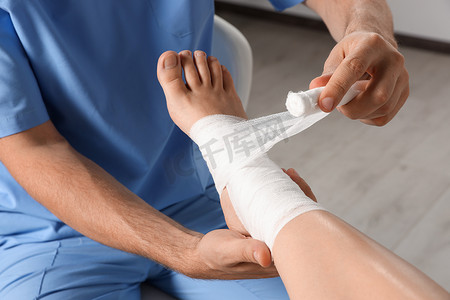 hospital摄影照片_Doctor applying bandage onto patient's foot in hospital, closeup