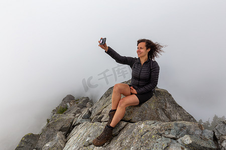 年轻的冒险女孩在崎岖的岩石山顶上，在多云的夏日早晨自拍。拍摄于加拿大不列颠哥伦比亚省北温哥华的皇冠山.