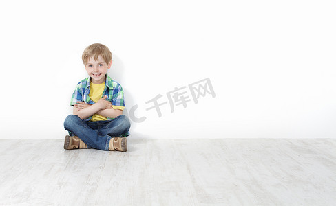 Handsome little boy sitting on floor leaning against white wall