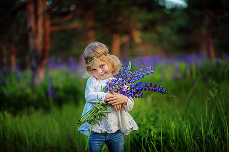漂亮的小女孩，与蓝色的花朵，在球场上。阳光。金色的头发.