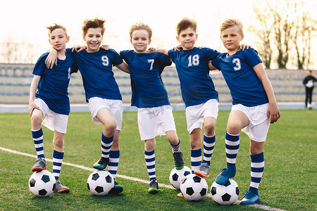 足球校队的体育男生。足球中的儿童团体泽西运动服站在草地球场上与球。快乐微笑运动队伍中的孩子