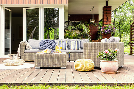 庭院桌与果子和新鲜橙汁站立在木露台与植物、扶手椅和沙发与枕头