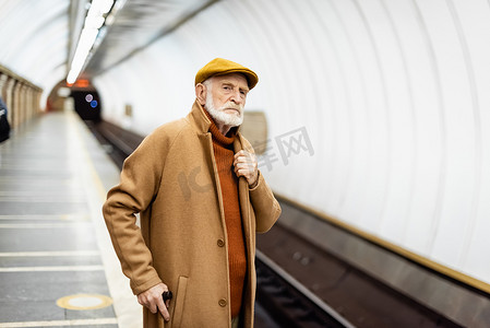 穿着秋装的老人一边摸着衣领一边望着地铁月台