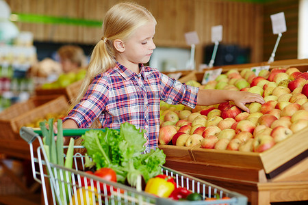 Cute little customer choosing the most tasty apple from assortment