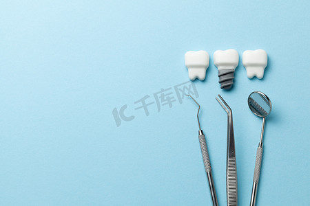 健康的白色牙齿和植入的蓝色背景和牙医工具镜子，钩。文本的复制空间.